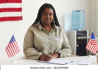 Portrait of smiling African-American woman working at at polling station on election day and registering voters, copy space