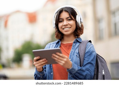 Portrait Of Smiling Arab Female Student In Wireless Headphones Using Digital Tablet Outdoors, Cheerful Middle Eastern Woman With Backpack Resting With Modern Gadget After College Classes, Copy Space - Shutterstock ID 2281489685