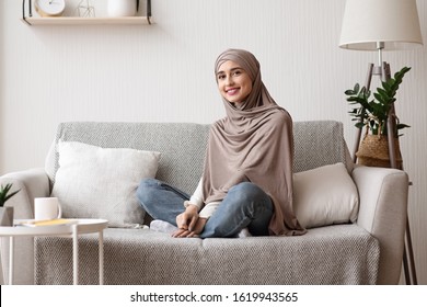 Portrait Of Smiling Arabic Girl In Hijab Posing On Sofa At Home, Relaxing On Comfortable Couch In Living Room, Enjoying Weekend