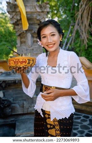 Portrait of smiling Asian Bali Woman with beauty face and attractive full lips wearing a white shirt and brown sarong in a temple