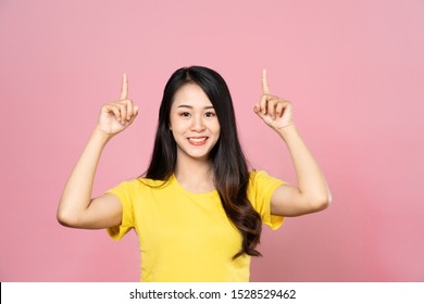 Portrait Of Smiling Asian Beautiful Young Woman Presenting With Two Hand Finger Point On Upper Side To Copy Space. The Girl Standing And Looking Up At In Studio. Advertisement & Presentation Concept.