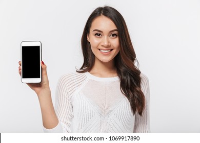 Portrait of a smiling asian businesswoman showing blank screen mobile phone isolated over white background