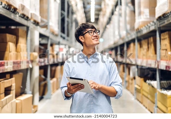 Portrait of\
smiling asian engineer foreman in helmets man order details\
checking goods and supplies on shelves with goods background in\
warehouse.logistic and business\
export