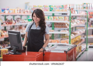 Portrait of smiling asian female staff standing at cash counter in supermarket