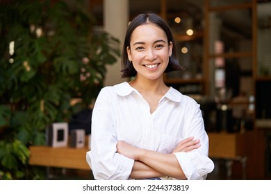 Portrait of smiling asian girl in white collar shirt, working in cafe, managing restaurant, looking confident and stylish.