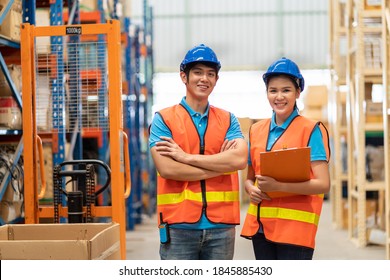 Portrait of smiling Asian male and female warehouse worker in safety vest and helmet standing with arms crossed, holding clipboard in storage warehouse with shelf pallet spare parts parcel background - Powered by Shutterstock