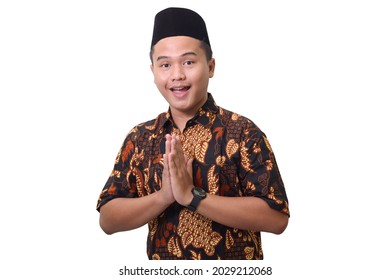 Portrait of smiling Asian man wearing batik shirt and songkok showing apologize and welcome hand gesture. Advertising concept. Isolated image on white background