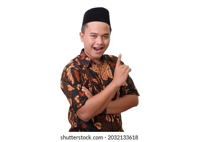 Portrait of smiling Asian man wearing batik shirt and songkok pointing up his forefinger and reminding something to do with crossed arm. Isolated image on white background