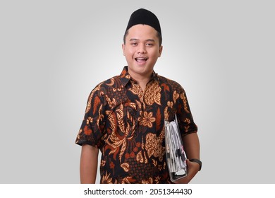 Portrait Of Smiling Asian Man Wearing Batik Shirt And Songkok Holding A Folder With Documents And Bills. Isolated Image On Gray Background