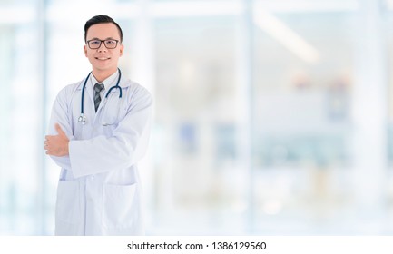 Portrait Of Smiling Asian Medical Male Doctor Standing In Front Of Blurred Interior Hospital Office Background.Concept Of Effective Work In Hospitals.