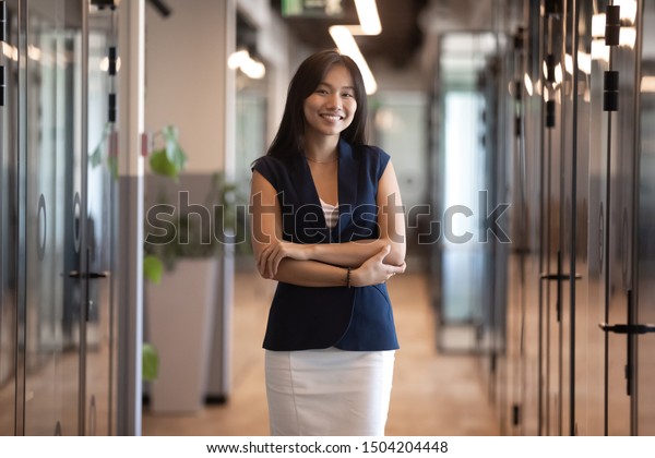 現代のオフィスの廊下に立ち ポーズをとって 自信満々の若い女性社員や上司が仕事場でカメラメーキを見る 微笑むアジアのミレニアルなビジネスマンのポートレート の写真素材 今すぐ編集