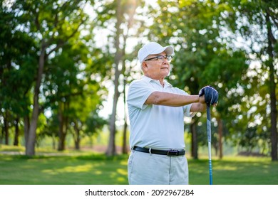 Portrait of Smiling Asian senior man golfer holding golf club standing on golf course in summer sunny day. Healthy elderly male enjoy outdoor lifestyle activity sport golfing at golf country club.
