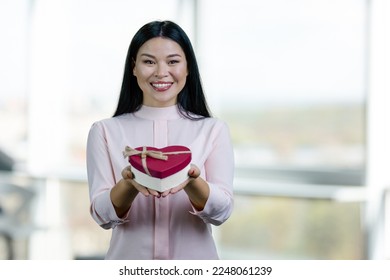 Portrait of smiling asian woman giving heart-shaped gift box. Bright indoor windows background. - Shutterstock ID 2248061239