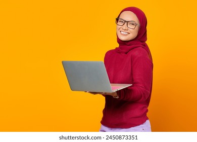 Portrait of smiling asian woman holding laptop over yellow background - Powered by Shutterstock