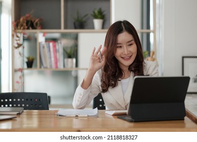 Portrait Of Smiling Asian Woman Waving Hello Talking On Video Call. Successful Young Woman Sitting White Suits. Business Conference Via Laptop