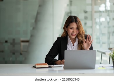 Portrait Of Smiling Asian Woman Waving Hello Talking On Video Call. Successful Young Woman Sitting White Suits. Business Conference Via Laptop