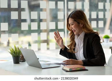 Portrait Of Smiling Asian Woman Waving Hello Talking On Video Call. Successful Young Woman Sitting White Suits. Business Conference Via Laptop