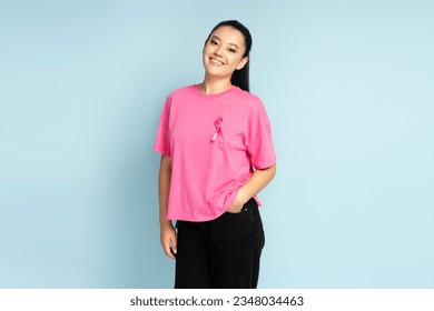 Portrait of  smiling asian woman wearing  t shirts with breast cancer pink ribbon looking at camera isolated on blue background. Health care, support, prevention. Breast cancer awareness month concept - Powered by Shutterstock