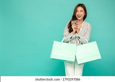 Portrait Of Smiling Asian Women Holding Credit Card And Green Shopping Bag Isolated Over Green Background, Happy Feeling Of Shopper Concept