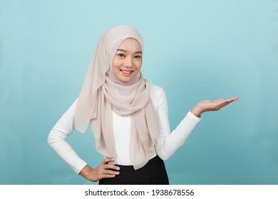 Portrait Of Smiling Asian Young Muslim Woman In Hijab Head Scarf Standing And Raising Her Hands Against Blue Colour Background