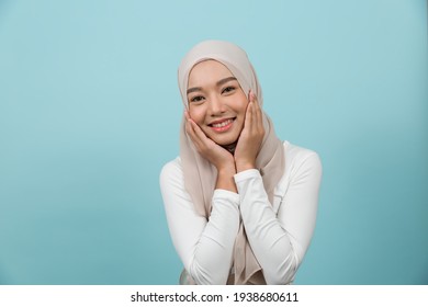 Portrait Of Smiling Asian Young Muslim Woman In Hijab Head Scarf Standing Against Blue Colour Background