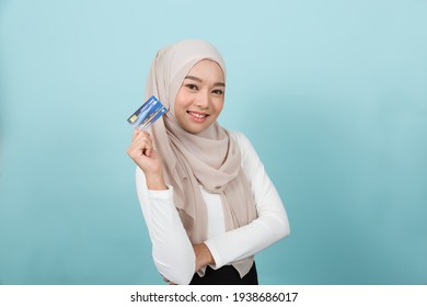 Portrait Of Smiling Asian Young Muslim Woman In Hijab Head Scarf Standing And Holding Credit Card Against Blue Colour Background