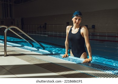 Portrait of smiling athletic female swimmer in professional swimsuit cap and glasses leaning on edge of swimming pool and looking at camera during training   - Powered by Shutterstock