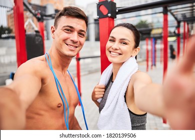 Portrait Of Smiling Athletic Man With Skipping Rope And Woman Taking Selfie After Workout In Open Air