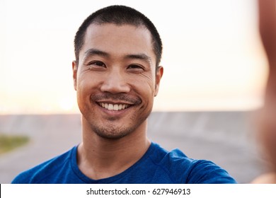 Portrait of a smiling athletic young Asian man in sportswear taking a selfie while out for an early morning run