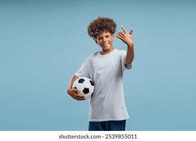 Portrait of smiling, attractive African American boy, teenager holding soccer ball, looking at camera isolated on blue background. Hobby concept - Powered by Shutterstock