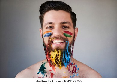 Portrait of smiling attractive bearded man with colorful painted beard on gray background - Shutterstock ID 1043492755