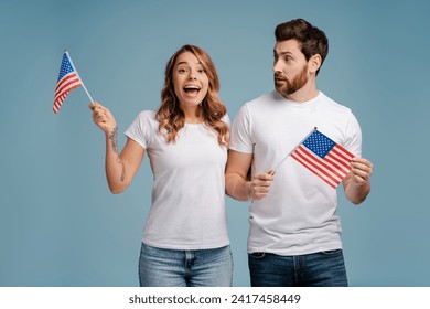 Portrait of smiling attractive couple, supporters holding American flags watching tv, waiting election results isolated on blue background. Vote day, election concept  - Powered by Shutterstock