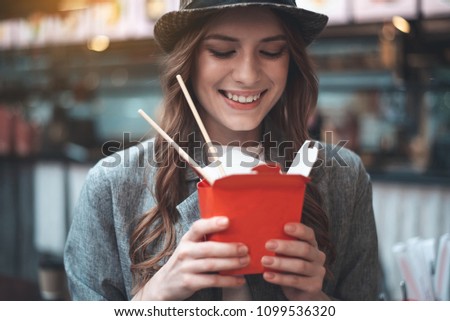 Portrait of smiling attractive lady holding a kind of oriental food. She is wearing hat and looking at her meals with excitement
