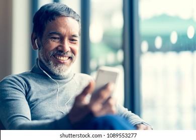 Portrait Smiling Attractive Mature Man Retired With White Stylish Short Beard Using Smartphone Or Listening Music And Sitting At Coffee Shop Cafe.  Old Man Using Social Network Internet Technology