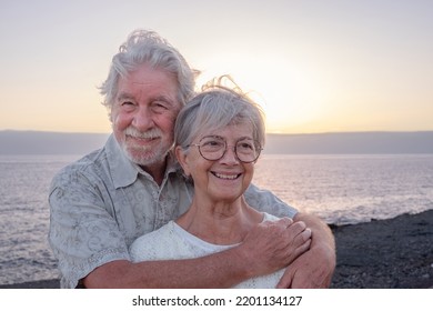 Portrait of smiling attractive senior couple embracing on the beach enjoying sea vacations - caucasian man and woman in love at sunset light - Powered by Shutterstock