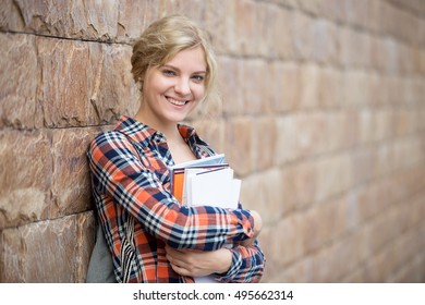 Portrait Of A Smiling Attractive Student With Books Against The Brick Wall. Back To School Concept Photo