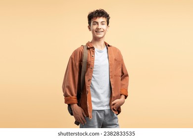 Portrait of smiling attractive teenage schoolboy with dental braces, wearing casual clothes, backpack on shoulder isolated on beige background. Education concept - Powered by Shutterstock