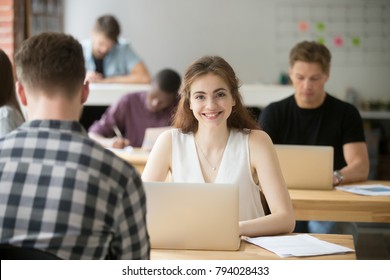 Portrait of smiling attractive woman looking at camera sitting at desk in co-working, young freelancer student intern employee working in shared office, businesswoman with laptop in coworking space