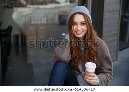 Portrait of smiling attractive young woman drinking coffee-to-go in the city