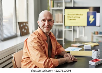 Portrait Of Smiling Bald Man Looking At Camera While Sitting At Workplace In Casual Office Setting