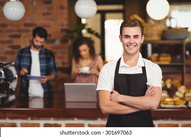 Portrait of smiling barista with arms crossed in front of customers at coffee shop - Powered by Shutterstock