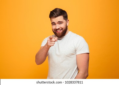 Portrait Of A Smiling Bearded Man Pointing Finger At Camera Isolated Over Yellow Background