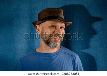 Portrait of a smiling bearded man wearing a hat. Isolated on blue background with shadow.