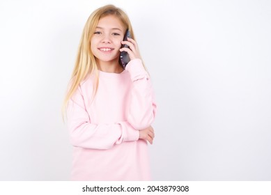 Portrait of a smiling beautiful caucasian little girl wearing pink sweater over white background talking on mobile phone. Business, confidence and communication concept.