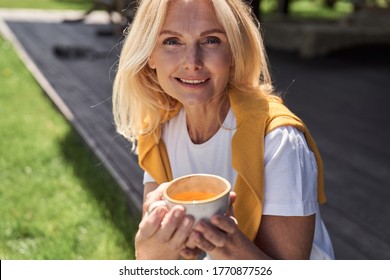 Portrait of smiling beautiful mature female relaxing in countryside yard with hot drink in morning - Powered by Shutterstock