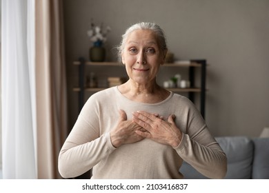 Portrait Of Smiling Beautiful Middle Aged 60s Woman Holding Folded Hands On Chest, Showing Appreciation, Feeling Thankful At Home. Happy Kind Old Mature Female Volunteer Expressing Love, Believe.