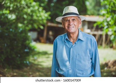 Portrait Of Smiling Beautiful Older Male Farmer. Elderly Man At Farm In Summer Day. Gardening Activity. Brazilian Elderly Man.