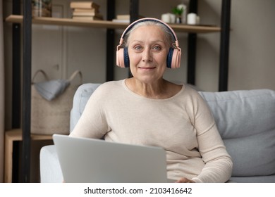 Portrait Of Smiling Beautiful Pleased Mature Retired Hoary Woman In Headphones Using Computer Applications, Communicating Distantly Or E-learning At Home, Older People And Modern Technology Usage.