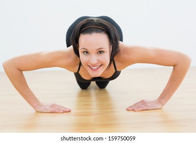 Portrait of a smiling beautiful sporty woman doing push ups in fitness studio