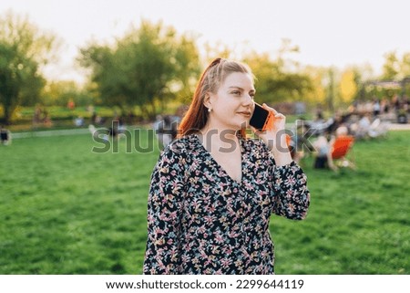 A portrait of a smiling beautiful woman talking on phone on nature background. Happy woman in dress is using a smartphone in park outdoors, summer time. Traveler